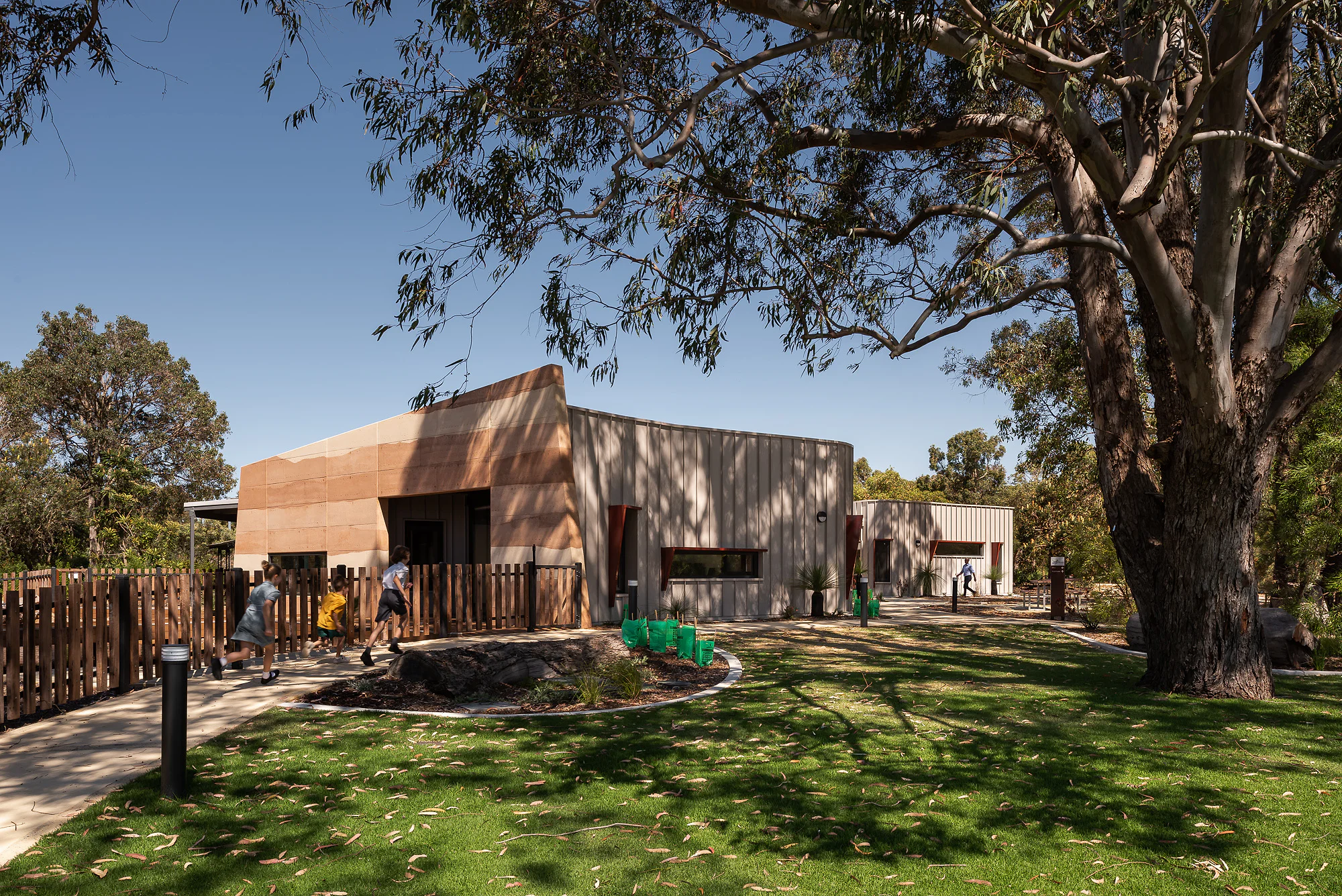 Precinct lawn framed by mature eucalypts with visitors and play structures