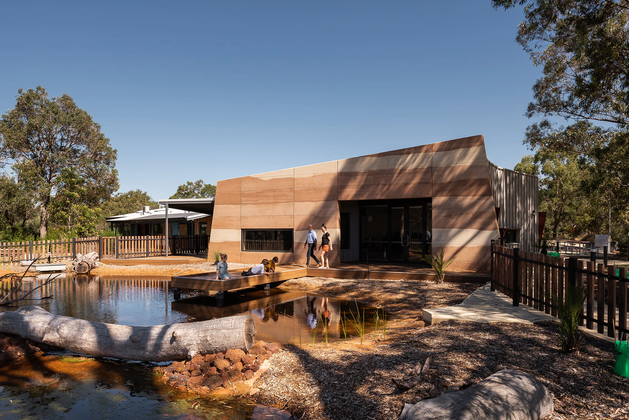 Precinct composition - terracotta education centre and white auxiliary building linked by timber fence