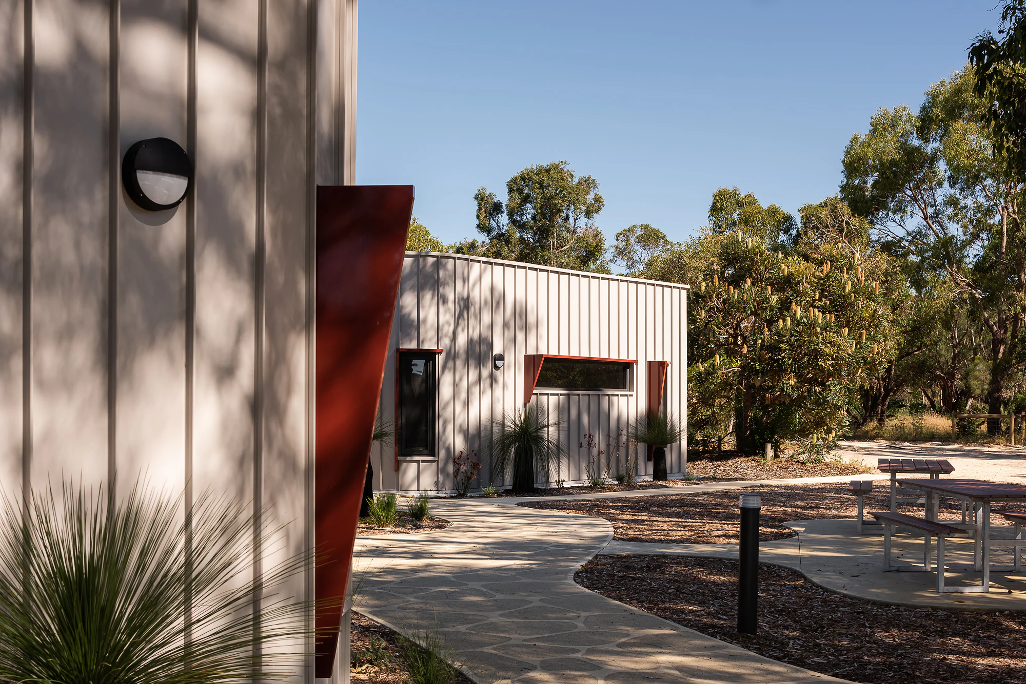 Sculptural red vertical element on white corrugated wall with circular window